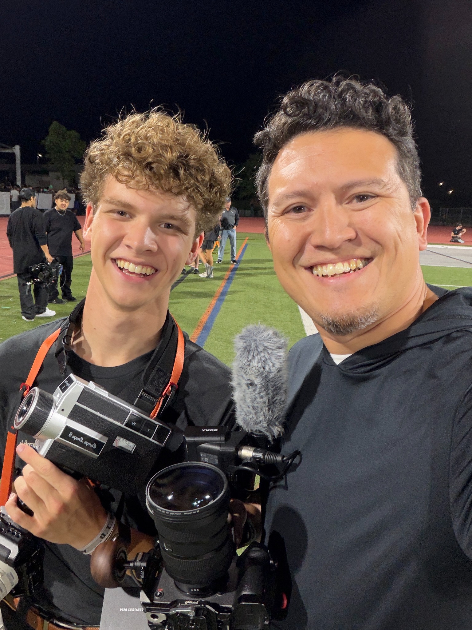 Two people with cameras and a microphone on location at night