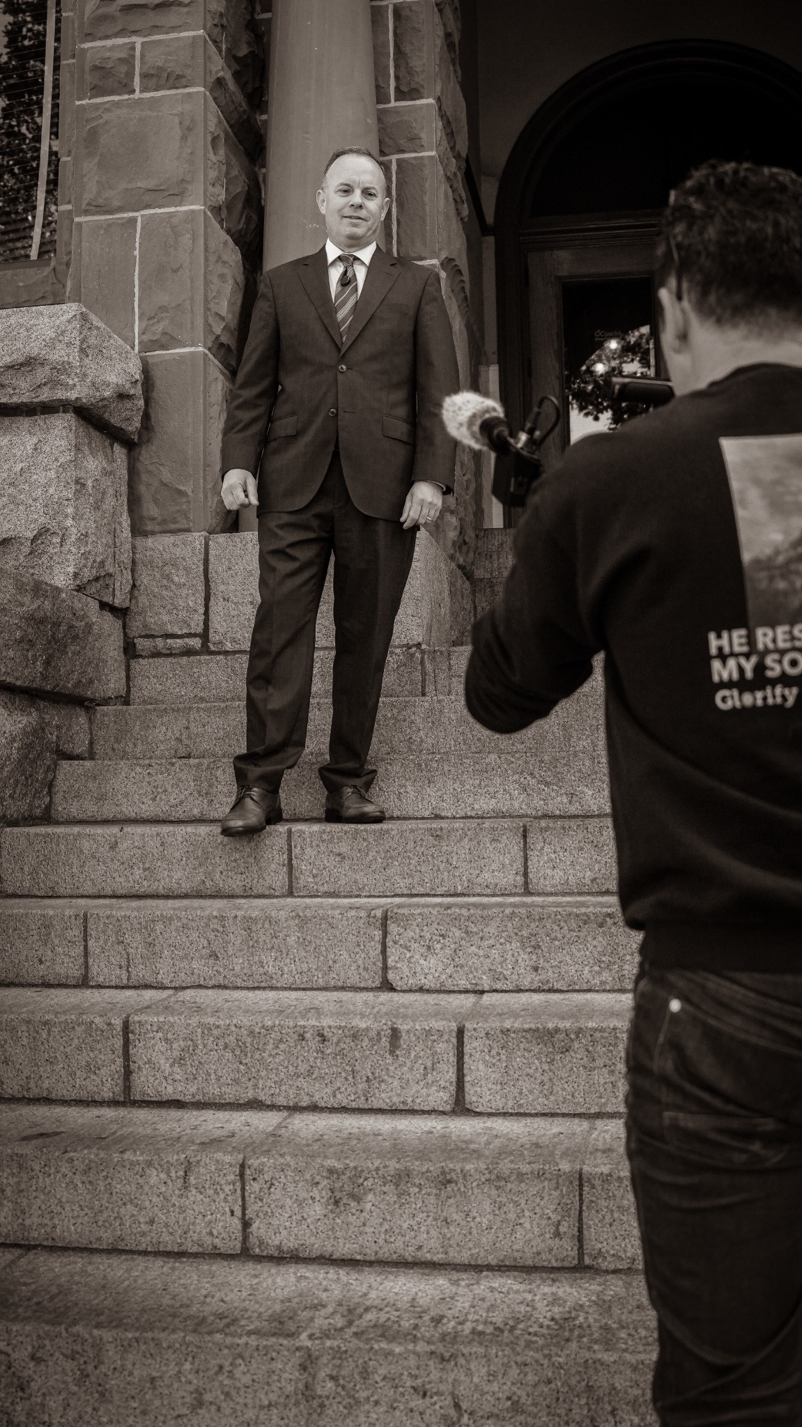 Camera operator filming a suited interview subject on stone steps